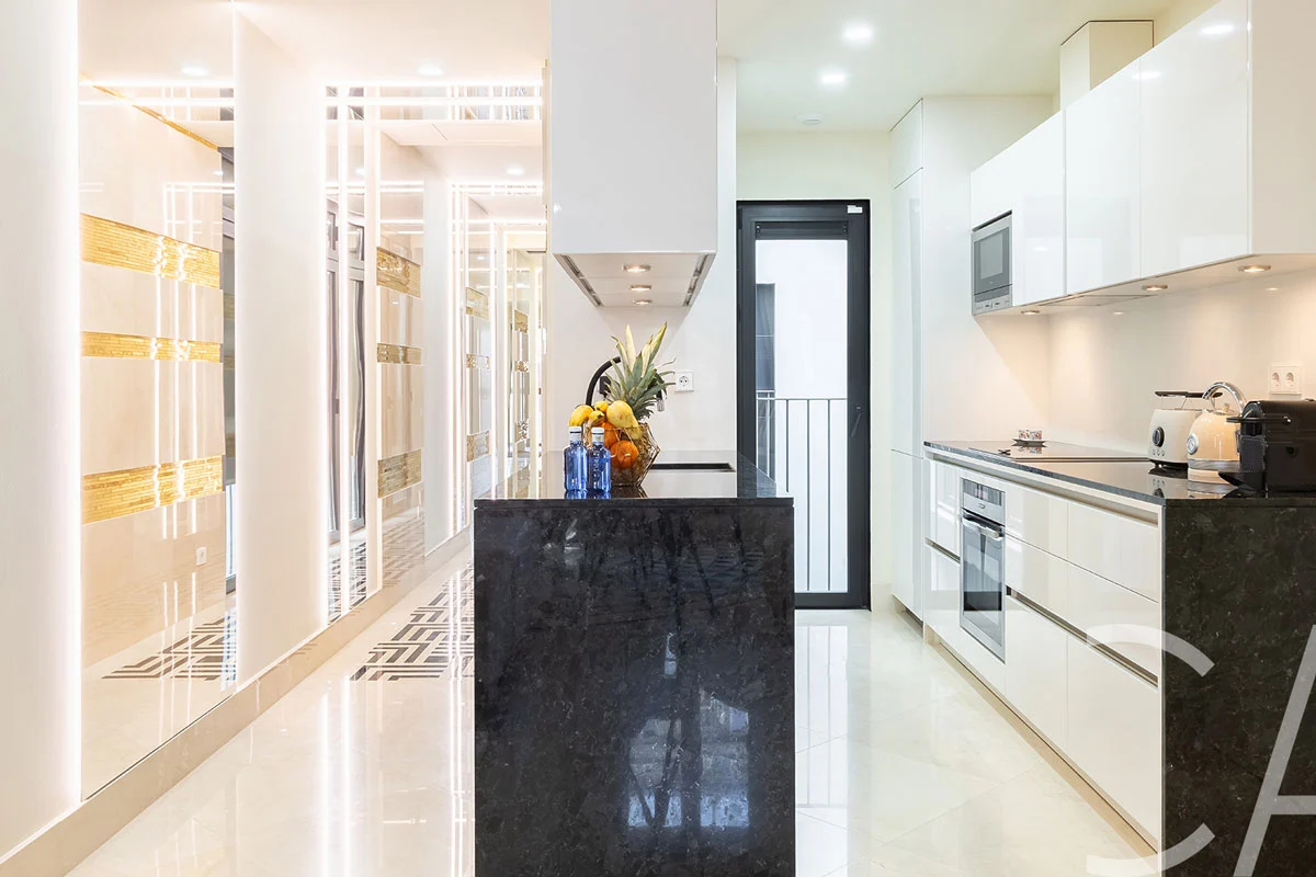 Salon de style Art déco doté de canapés en cuir, parfaitement intégré à une cuisine entièrement équipée, créant ainsi un vaste espace de vie dans un appartement de luxe à louer sur la Rambla Catalunya, dans le quartier de l'Eixample, à Barcelone.